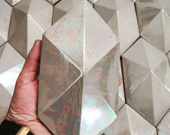 Pode incluir: Um único azulejo de cerâmica branco iridescente com um design geométrico facetado. O azulejo tem a forma de um diamante e um acabamento brilhante.