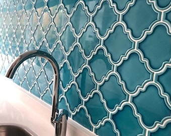 May include: A close-up of a teal blue kitchen backsplash with a geometric pattern. The backsplash is made of small, square tiles with a raised, white design. A chrome faucet is in the foreground.