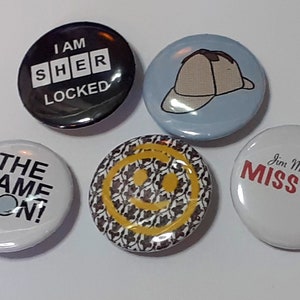 Puede incluir: Un conjunto de cinco botones redondos. Un botón negro dice "I AM SHER LOCKED" en blanco. Otros botones muestran un sombrero de detective, una carita sonriente y las frases "THE GAME IS ON!" y "Jim Moriarty MISS ME?"