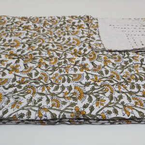 May include: A white cotton quilt with a floral pattern in shades of green and yellow. The quilt is folded in thirds and has a small matching pillow.