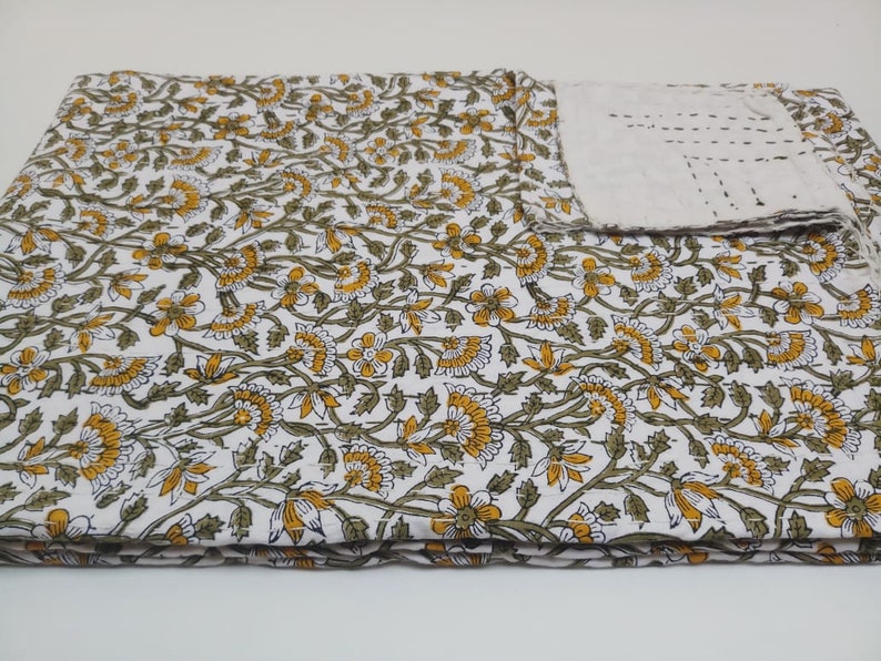May include: A white cotton quilt with a floral pattern in shades of green and yellow. The quilt is folded in thirds and has a small matching pillow.