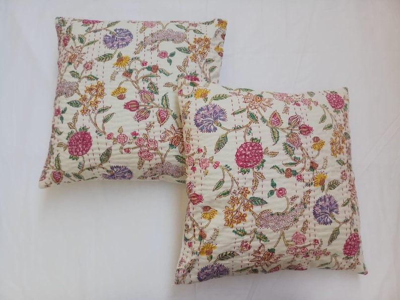 May include: Two white cotton pillow covers with a floral print in shades of pink, purple, yellow, and green. The floral pattern features delicate flowers and leaves on a white background.