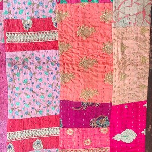 Pode incluir: Uma colcha de retalhos feita de v&aacute;rios tecidos em tons de rosa, vermelho e p&ecirc;ssego. A colcha &eacute; decorada com bordados dourados e padr&otilde;es florais.