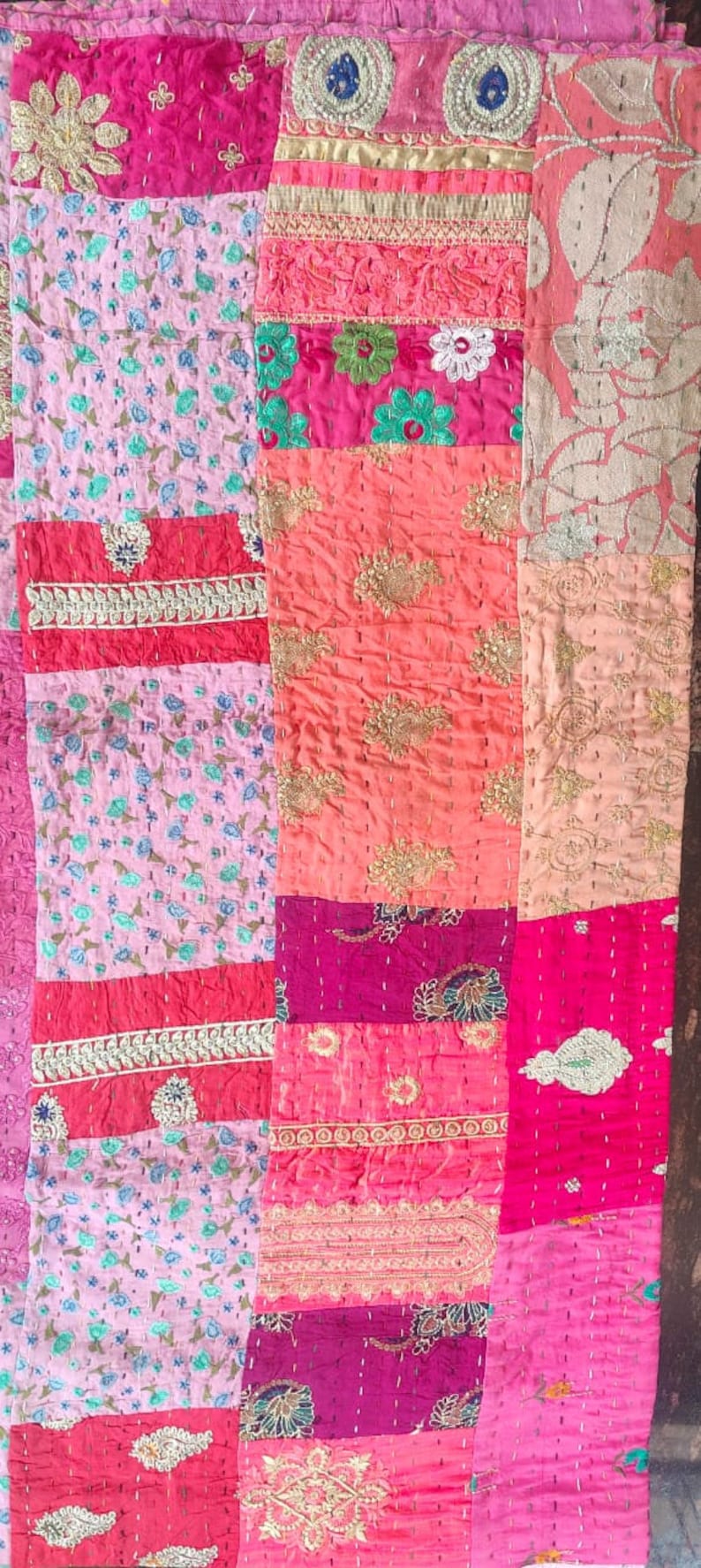Pode incluir: Uma colcha de retalhos feita de v&aacute;rios tecidos em tons de rosa, vermelho e p&ecirc;ssego. A colcha &eacute; decorada com bordados dourados e padr&otilde;es florais.