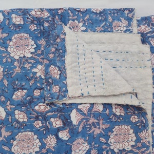 May include: A blue and white kantha quilt with a floral pattern. The quilt is folded in half and the stitching is visible.