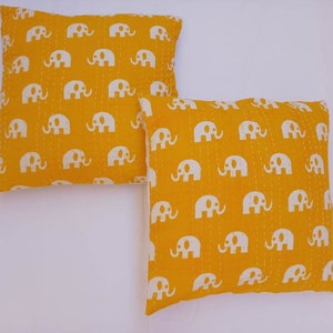 May include: Two yellow throw pillows with white elephant print. The pillows are made of cotton and have a quilted design.