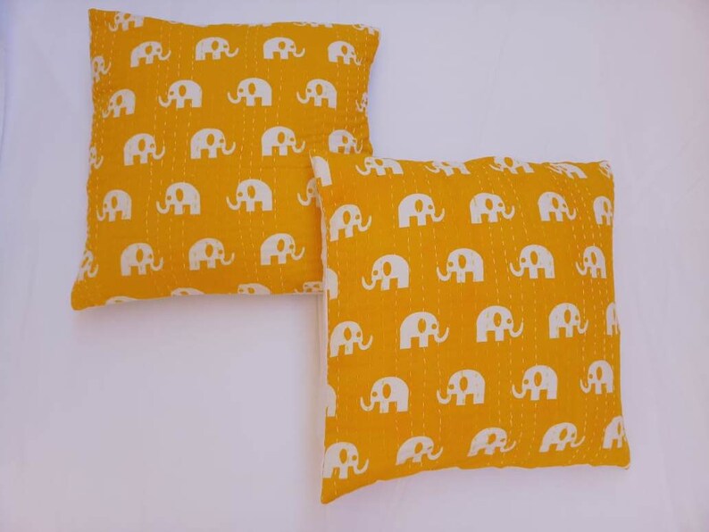 May include: Two yellow throw pillows with white elephant print. The pillows are made of cotton and have a quilted design.