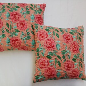 May include: Two peach-colored throw pillows with a floral pattern of pink roses and green leaves. The pillows are quilted and have a subtle sheen.