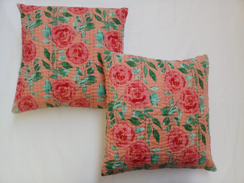 May include: Two peach-colored throw pillows with a floral pattern of pink roses and green leaves. The pillows are quilted and have a subtle sheen.