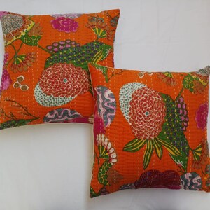 May include: Two orange cotton pillow covers with a floral pattern in shades of pink, green, and blue. The pillow covers are quilted and have a white border.