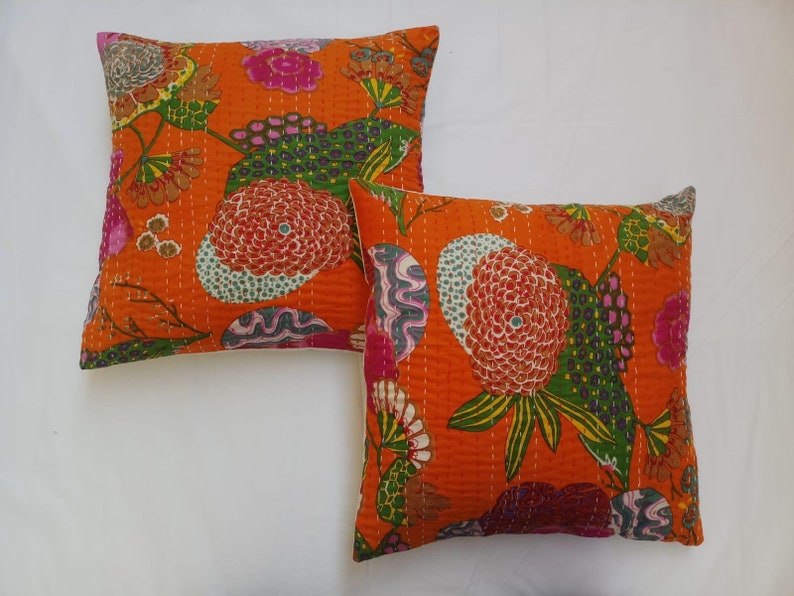May include: Two orange cotton pillow covers with a floral pattern in shades of pink, green, and blue. The pillow covers are quilted and have a white border.