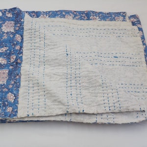 May include: A blue and white kantha quilt with a floral print on one side and a white side with blue stitching. The quilt is folded in half.