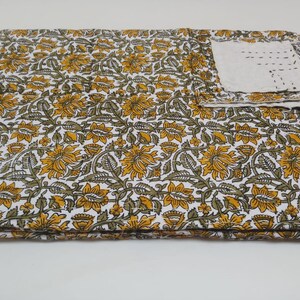 May include: A white cotton fabric with a floral pattern in shades of yellow and green. The fabric is folded in thirds and a small white square of fabric is visible in the upper right corner.