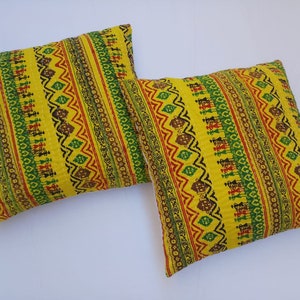May include: Two yellow throw pillows with a colorful geometric pattern. The pattern features red, green, and black stripes with a repeating design.