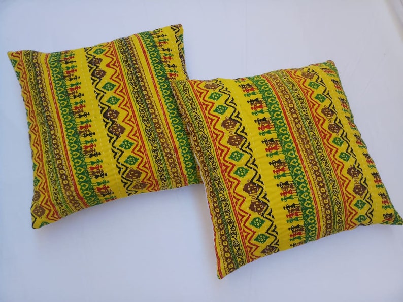 May include: Two yellow throw pillows with a colorful geometric pattern. The pattern features red, green, and black stripes with a repeating design.