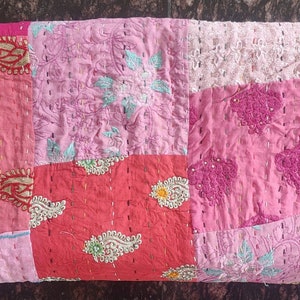 Pode incluir: Uma colcha de retalhos com uma variedade de tecidos rosa e vermelho. A colcha &eacute; feita de diferentes peda&ccedil;os de tecido costurados juntos, e tem um design floral.