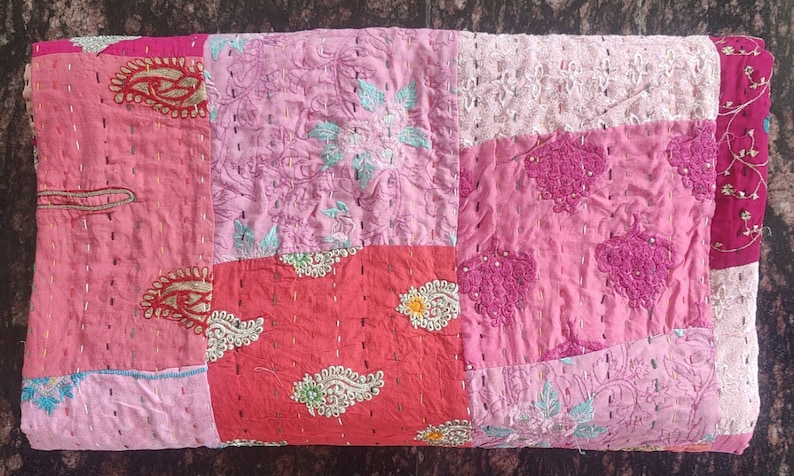 Pode incluir: Uma colcha de retalhos com uma variedade de tecidos rosa e vermelho. A colcha &eacute; feita de diferentes peda&ccedil;os de tecido costurados juntos, e tem um design floral.