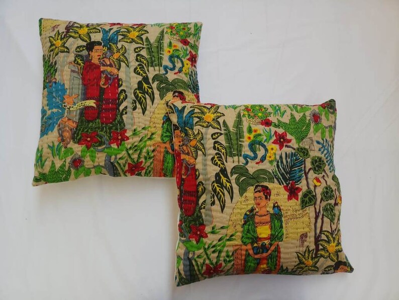 May include: Two square throw pillows with a beige background and a colorful floral pattern. The pattern includes green leaves, red flowers, and images of women with dark hair and colorful clothing.