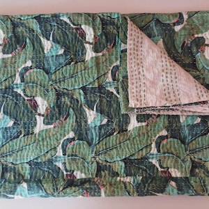 May include: A green and white kantha quilt with a leaf pattern. The quilt is folded in half and the back side is visible.