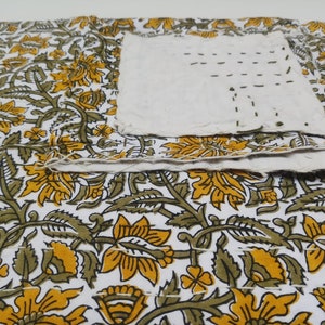 May include: A white fabric with a floral pattern in shades of yellow and green. The fabric is folded over itself and has visible stitching.