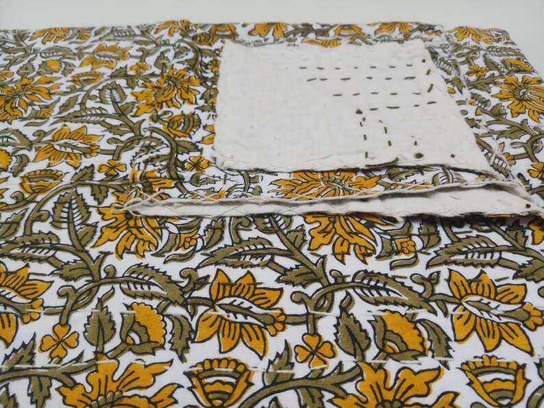 May include: A white fabric with a floral pattern in shades of yellow and green. The fabric is folded over itself and has visible stitching.