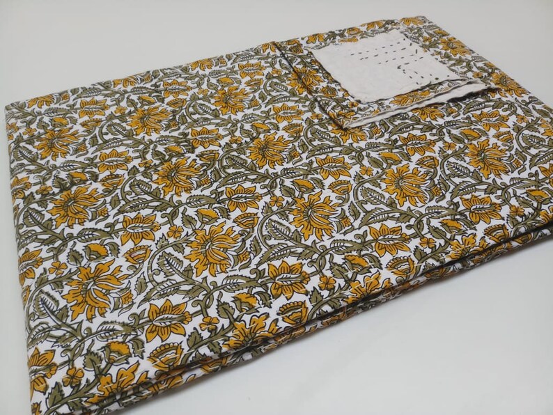 May include: A white cotton fabric with a yellow and green floral print. The fabric is folded in half and has a small white square of fabric on top.