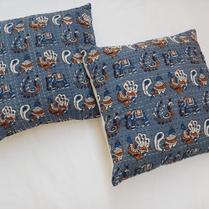 May include: Two blue and white patterned throw pillows with a design of peacocks and elephants. The pillows are made of cotton and have a quilted texture.