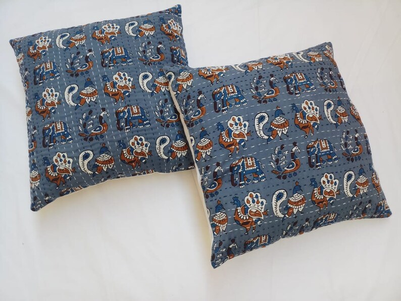 May include: Two blue and white patterned throw pillows with a design of peacocks and elephants. The pillows are made of cotton and have a quilted texture.