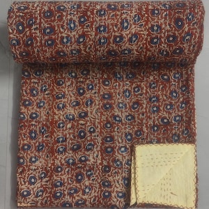 Könnte beinhalten: Eine rote und blaue florale Kantha-Steppdecke mit gelber Baumwollrückseite. Die Steppdecke ist aufgerollt und eine Ecke der Rückseite ist sichtbar.