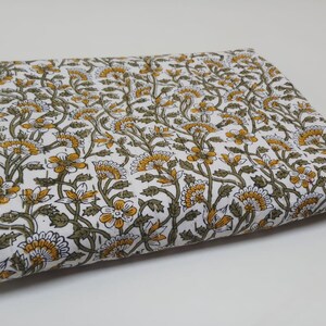 May include: White cotton fabric with a floral print in shades of green and yellow. The fabric is folded in half and has a smooth texture.