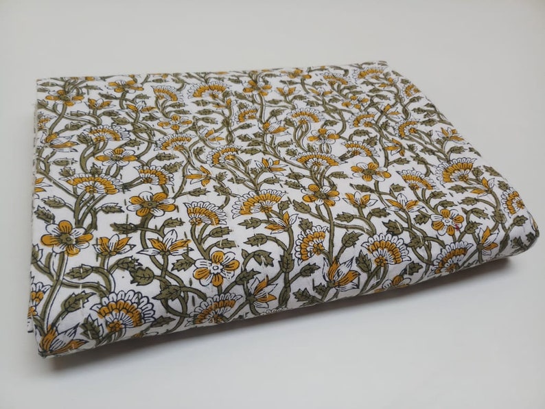 May include: White cotton fabric with a floral print in shades of green and yellow. The fabric is folded in half and has a smooth texture.