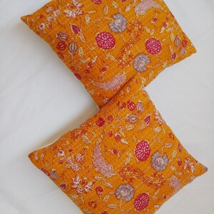 May include: Two yellow throw pillows with a floral pattern in shades of pink, white, and gray. The pillows are made of cotton and have a quilted texture.