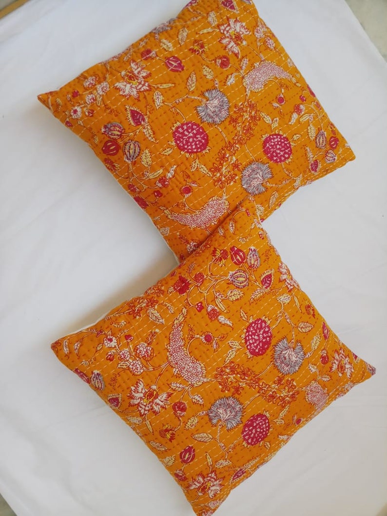 May include: Two yellow throw pillows with a floral pattern in shades of pink, white, and gray. The pillows are made of cotton and have a quilted texture.
