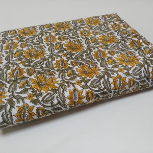 May include: White fabric with a yellow and green floral print. The fabric is folded in half and the print is visible on both sides.