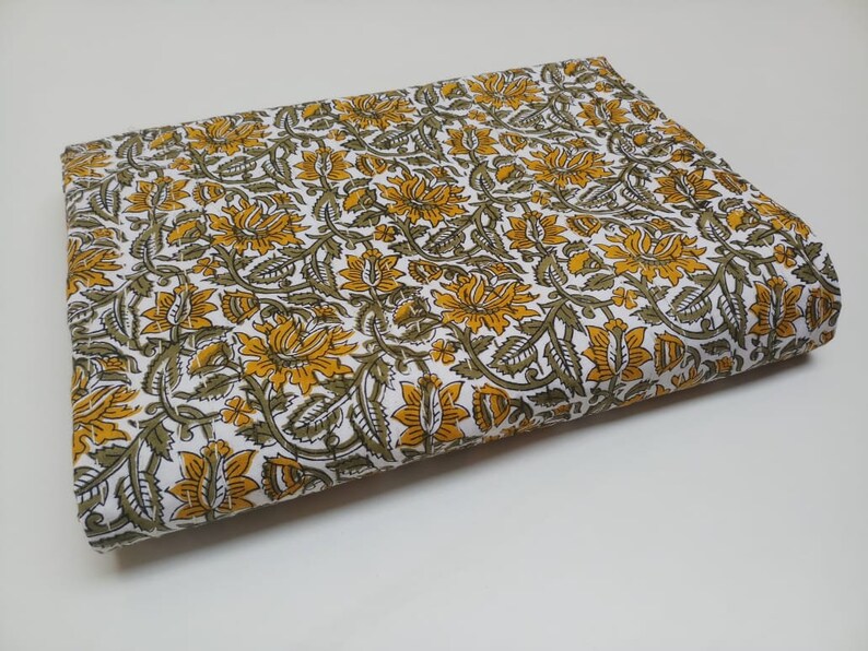 May include: White fabric with a yellow and green floral print. The fabric is folded in half and the print is visible on both sides.