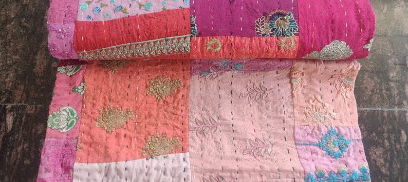 Pode incluir: Uma colcha de retalhos feita de v&aacute;rios tons de rosa e vermelho com detalhes intrincados de bordado. A colcha &eacute; feita de saris reciclados e &eacute; uma pe&ccedil;a de arte &uacute;nica e bela.