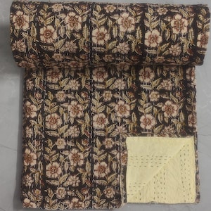 Puede incluir: Una colcha kantha negra con un patrón floral en tonos marrones y crema. La colcha está doblada por la mitad y los bordes son visibles. La colcha está hecha de algodón y está cosida a mano.