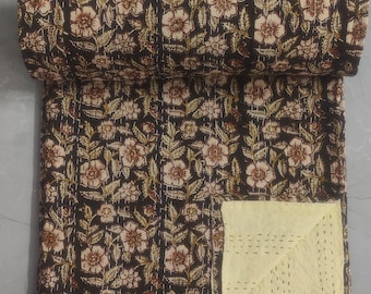 May include: A black kantha quilt with a floral pattern in shades of brown and cream. The quilt is folded in half and the edges are visible. The quilt is made of cotton and is hand-stitched.