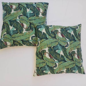 May include: Two green and white patterned throw pillows with a banana leaf design. The pillows are made of cotton and have a quilted texture.
