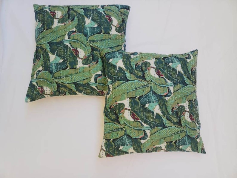 May include: Two green and white patterned throw pillows with a banana leaf design. The pillows are made of cotton and have a quilted texture.