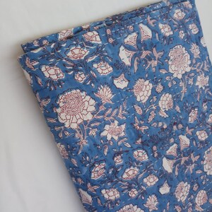 May include: A blue cotton quilt with a white and red floral pattern. The quilt is folded in half and has a quilted texture.