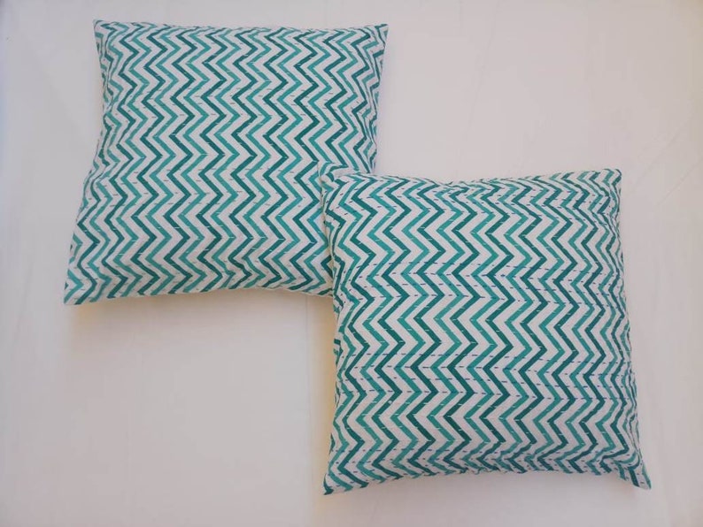 May include: Two green and white chevron patterned throw pillows. The pillows are made of a soft, cotton fabric and have a subtle sheen.