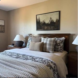 Peut inclure: Intérieur de chambre avec un lit en bois et une tête de lit, orné d'oreillers aux textures et motifs variés. Le lit est recouvert d'une couette blanche et d'une couverture grise à motifs. Une peinture de paysage encadrée est accrochée au-dessus du lit.
