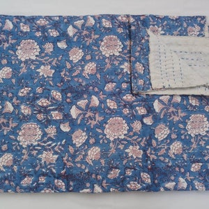 May include: A blue and white floral kantha quilt with a white backing. The quilt is folded in half and has a hand-stitched design.