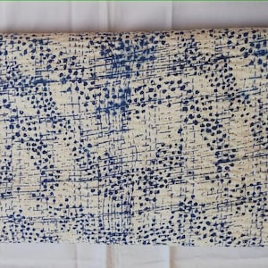 May include: Folded textile with a cream-colored background and a pattern of navy blue dots and lines. The fabric appears to be cotton or a similar material, and the pattern is evenly distributed across the surface.