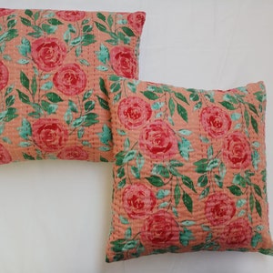 May include: Two peach-colored throw pillows with a floral pattern of pink roses and green leaves. The pillows are quilted and have a subtle sheen.