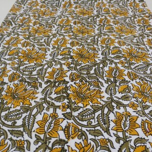May include: White fabric with a repeating pattern of yellow and green floral designs. The fabric has a quilted texture.