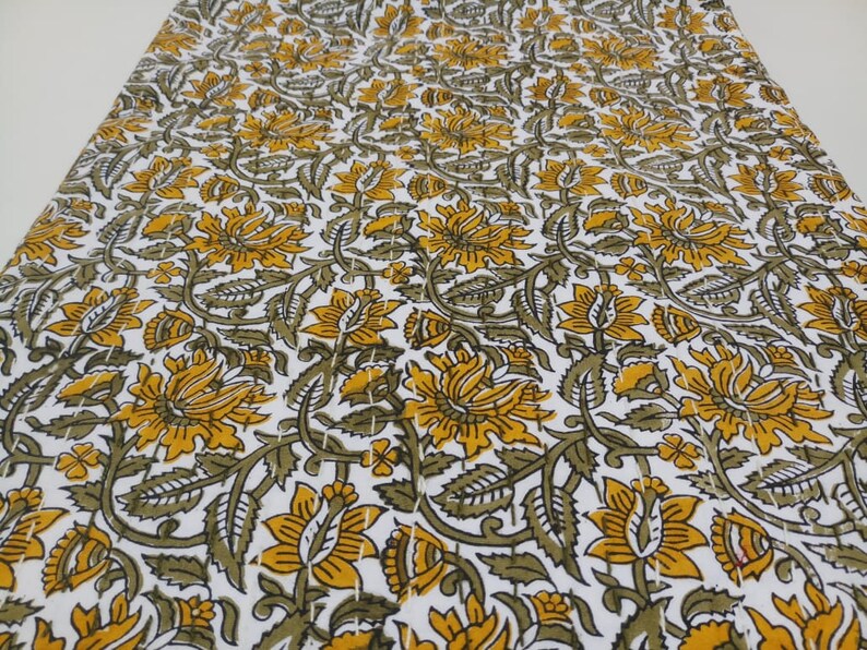 May include: White fabric with a repeating pattern of yellow and green floral designs. The fabric has a quilted texture.