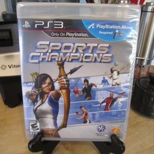 May include: A PlayStation 3 game case for "Sports Champions" with a blue, white, and silver design. The front of the case features a woman holding a bow and arrow, and the text "PlayStation Move Required" is displayed in the upper right corner.