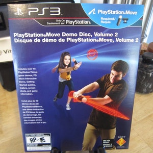 May include: PlayStation Move Demo Disc, Volume 2 for PS3. The cover features two people playing games with the PlayStation Move controller. The cover is blue with red and white accents. The text on the cover is in both English and French.